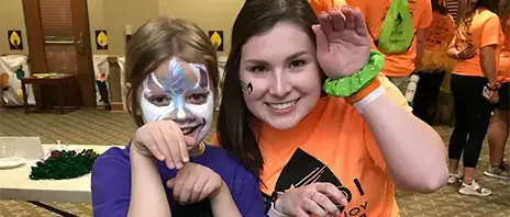 A smiling woman posing with a child with a painted face